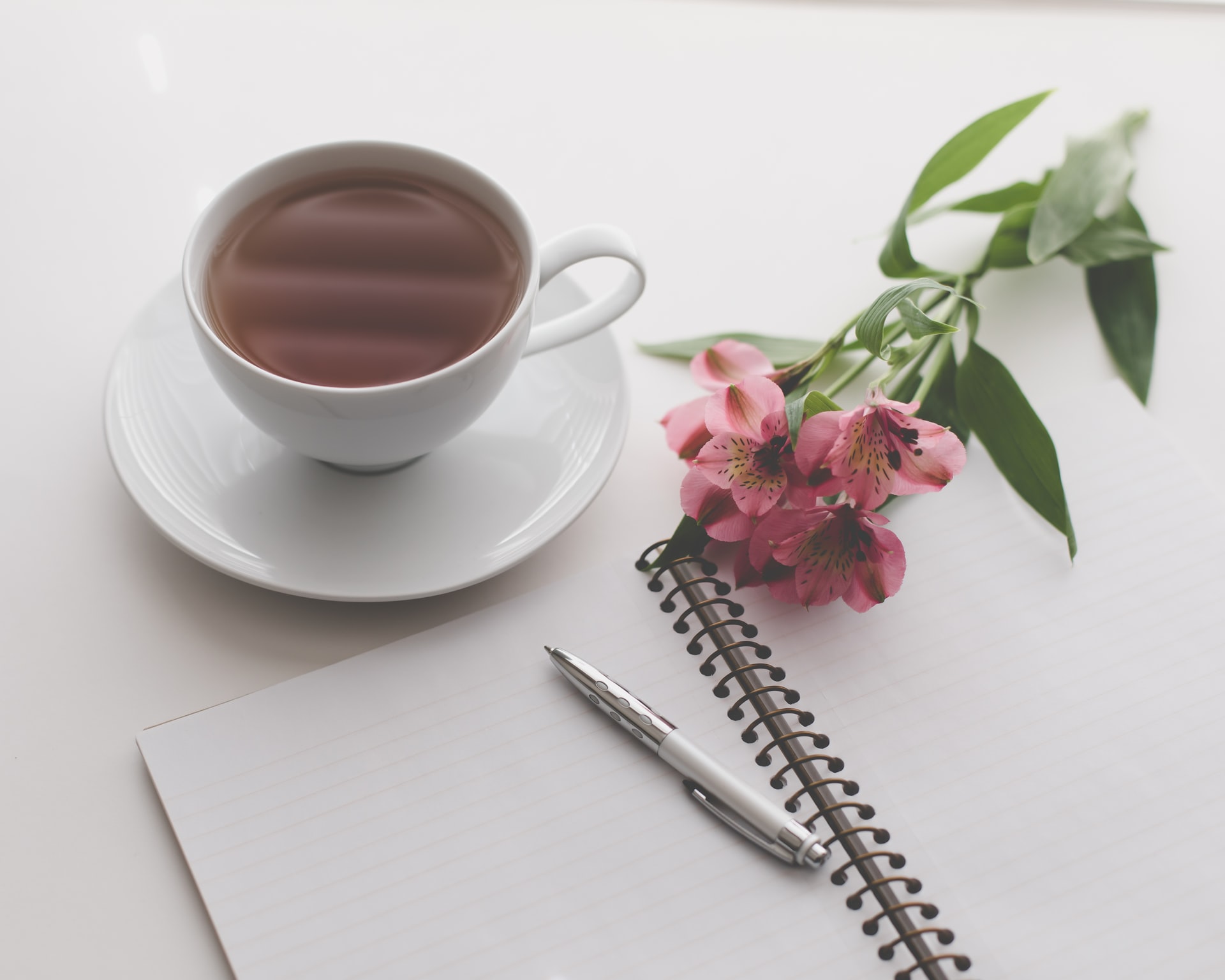 Cahier d'écriture à coté d'une tasse de thé et d'une fleur